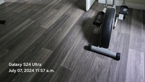 A room with grey wooden flooring, a stationary bike, and a door leading to another room. - This is a family-friendly place. (Dartmouth)