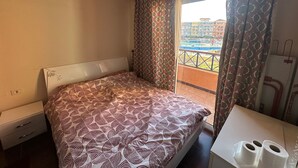 Habitación de hotel con cama, una mesita con dos rollos de papel higiénico, una ventana con cortinas estampadas y vistas a un conjunto de edificios.