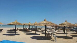 Una playa con hileras de sombrillas de paja y sillones de descanso.
