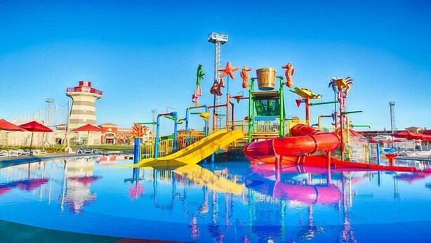 Parque acuático con un tobogán amarillo central, toboganes acuáticos rojos y una piscina reflectante.