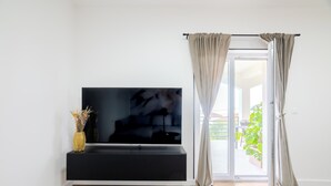 Un salon moderne avec un téléviseur à écran plat fixé sur une console noire, une porte-fenêtre coulissante avec des rideaux et un plancher en bois.