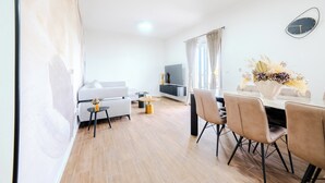 Un salon moderne avec un canapé, une table basse et un téléviseur. Il y a également un coin repas avec des chaises et une table.