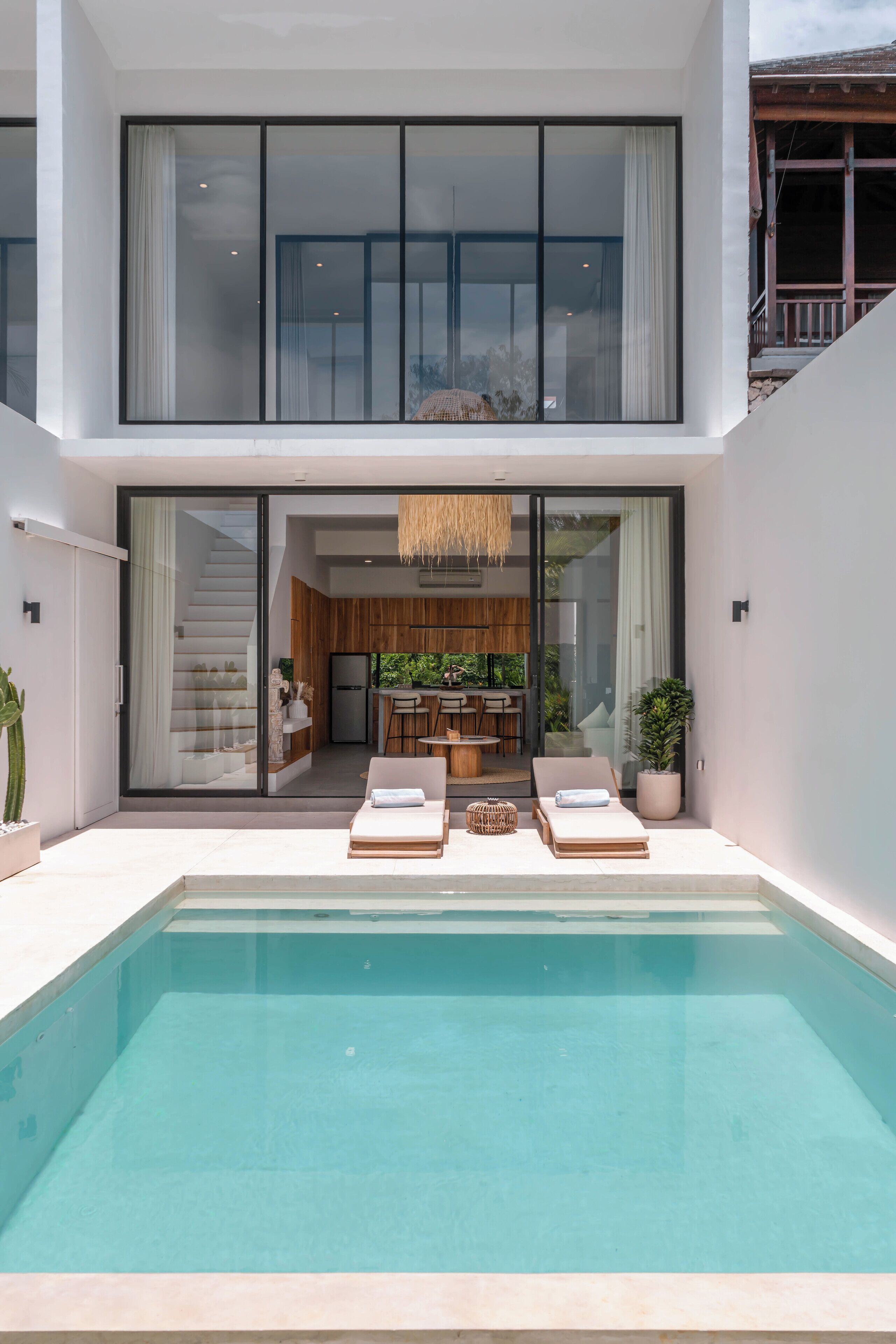 A modern house with a swimming pool, a kitchen, and a dining area visible through glass doors.