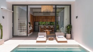 A modern house with a swimming pool, a kitchen, and a dining area visible through glass doors. - Villa Finity B (Canggu)