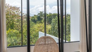 A bedroom with a large window, a bed, and a wicker chair. - Villa Finity B (Canggu)