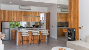 A modern kitchen with wooden cabinets, a central island with bar stools, a built-in oven, and a refrigerator. - Villa Finity B (Canggu)