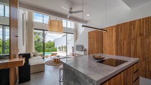 A modern kitchen with a large island, wooden accents, and a view of the outdoors. - Villa Finity B (Canggu)