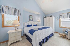 A bedroom with a bed, nightstand, lamp, and a window with blinds. - Searenity | 810 ft to the beach | Private Pool, Hot Tub, and Dog Friendly (Corolla)