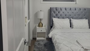 Een slaapkamer met een bed, een nachtkastje, een lamp, een raam met zonwering en een deur.