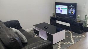 Een moderne woonkamer met een zwarte leren bank, een glazen salontafel en een flatscreen televisie op een zwart dressoir.