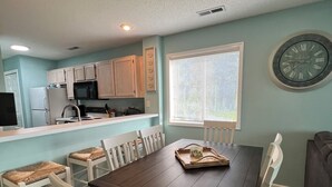 A dining area with a dark wooden table, white chairs, and a clock on the wall. - Waterway Haven (North Myrtle Beach)