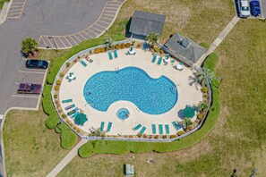 An aerial view of a swimming pool with a circular shape, surrounded by a white fence, and adjacent to a parking area. - Waterway Haven (North Myrtle Beach)