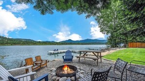 Terraza frente al lago con sillas Adirondack, un pozo de fuego y una mesa de madera.