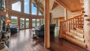 Interior espacioso de una cabaña de troncos con una amplia sala de estar, una escalera de madera y vistas al exterior.