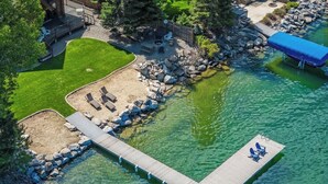 Vista aérea de un muelle que se adentra en aguas cristalinas, rodeado de jardines con asientos y una estructura cubierta.