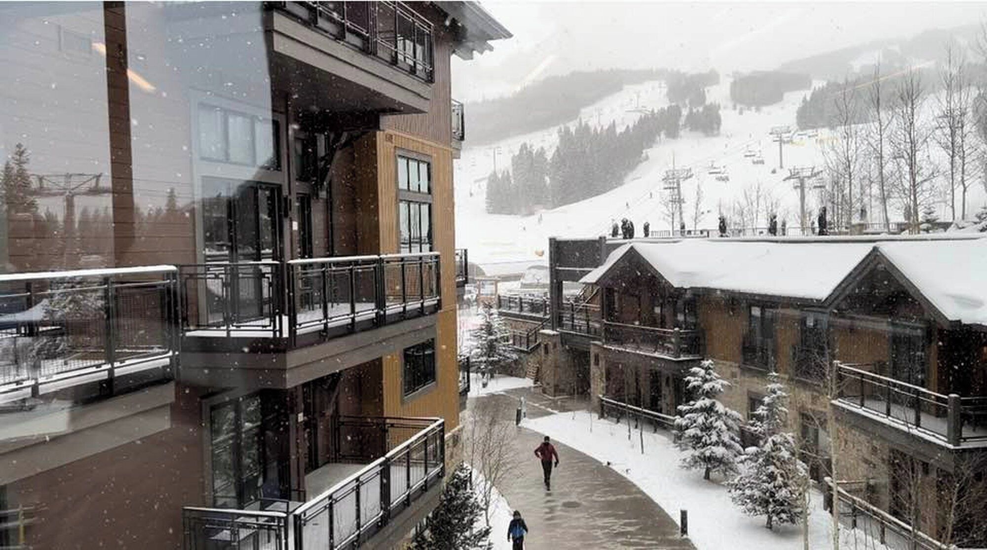 Un edificio a più piani con balconi, terreno innevato e una pista da sci sullo sfondo.