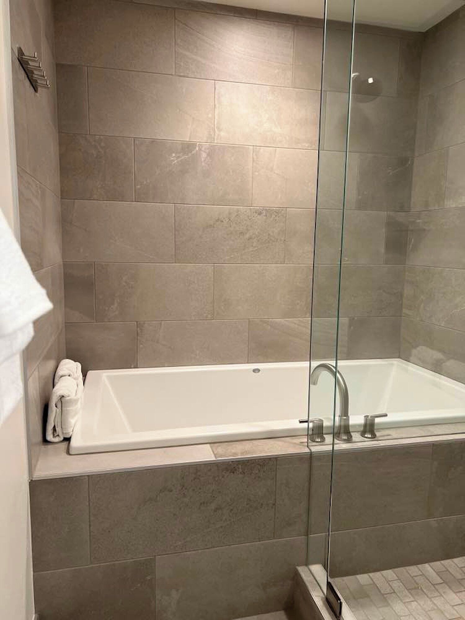 Une salle de bain moderne avec une douche à parois de verre, une baignoire blanche et des carreaux de couleur beige.