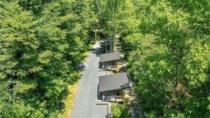 Un chalet isolé, accessible par un chemin de gravier, entouré d’une forêt dense.