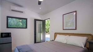 Une chambre avec un lit, une fenêtre, un appareil de climatisation, un four à micro-ondes et une porte donnant sur l’extérieur.
