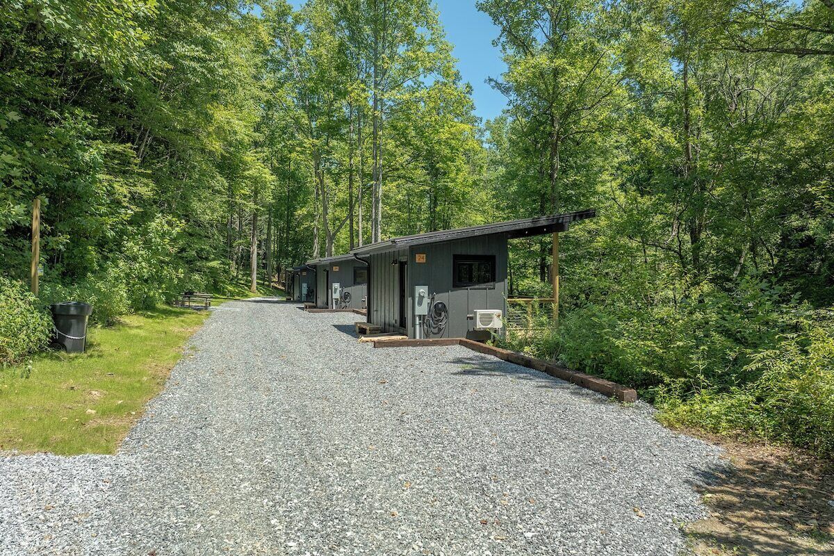 Un sentier de gravier mène à une rangée de cabanes entourées d’une forêt dense.