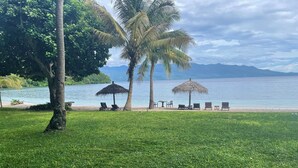 Een gazon met palmbomen, een strand en uitzicht op zee en bergen.