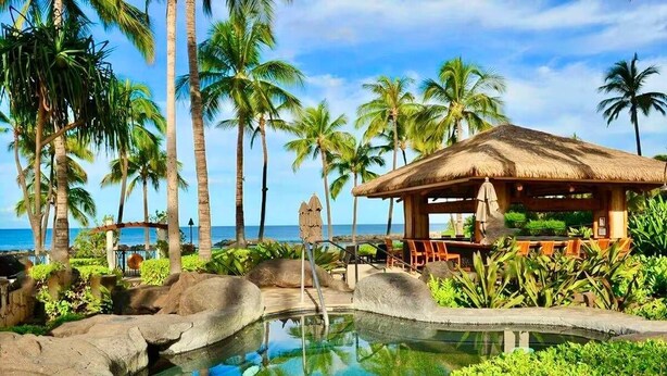 Un complexe hôtelier tropical doté d’une piscine entourée de palmiers et d’un pavillon à toit de chaume.