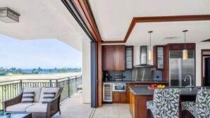 Un balcon avec vue sur la plage, une cuisine équipée d’appareils modernes et un espace salon extérieur.
