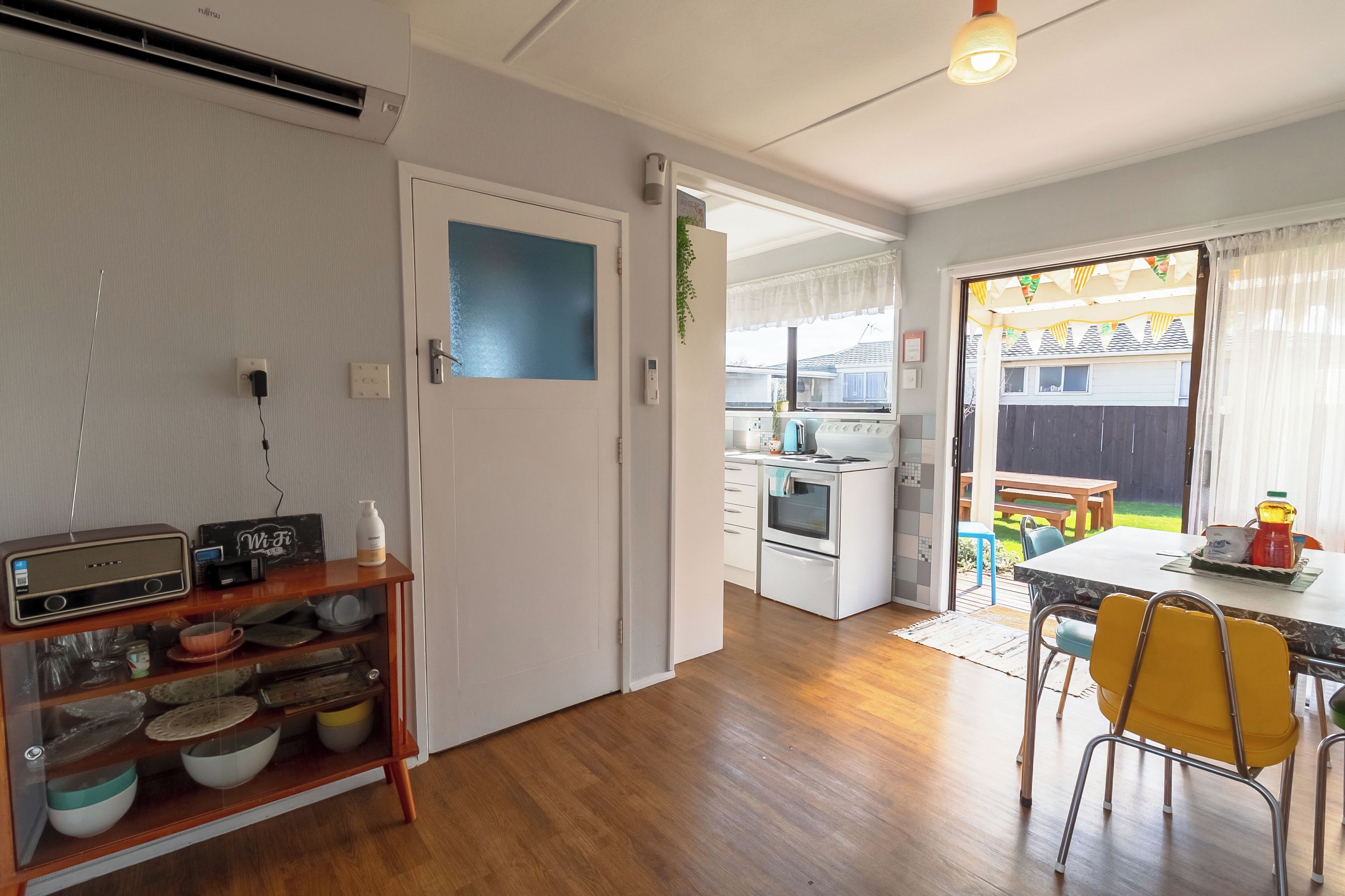 A kitchen with a wooden cabinet, a white door, and a dining area with yellow chairs.