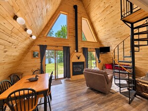 A cozy cabin interior with a dining area, a fireplace, a sofa, and a staircase.