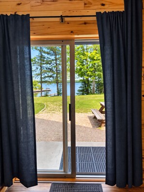 A room with a sliding glass door leading to an outdoor area with a picnic table and a view of a lake surrounded by trees.