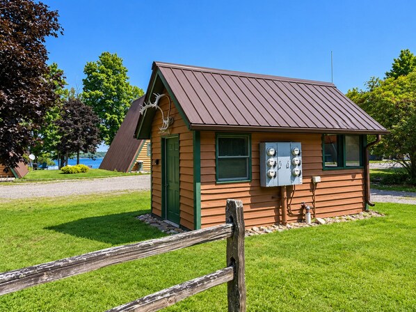 A small wooden cabin with a sloped roof, a green door, and a utility box.