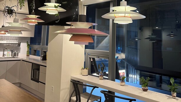 Une cuisine moderne avec des luminaires suspendus, un coin repas offrant une vue agréable et diverses plantes.