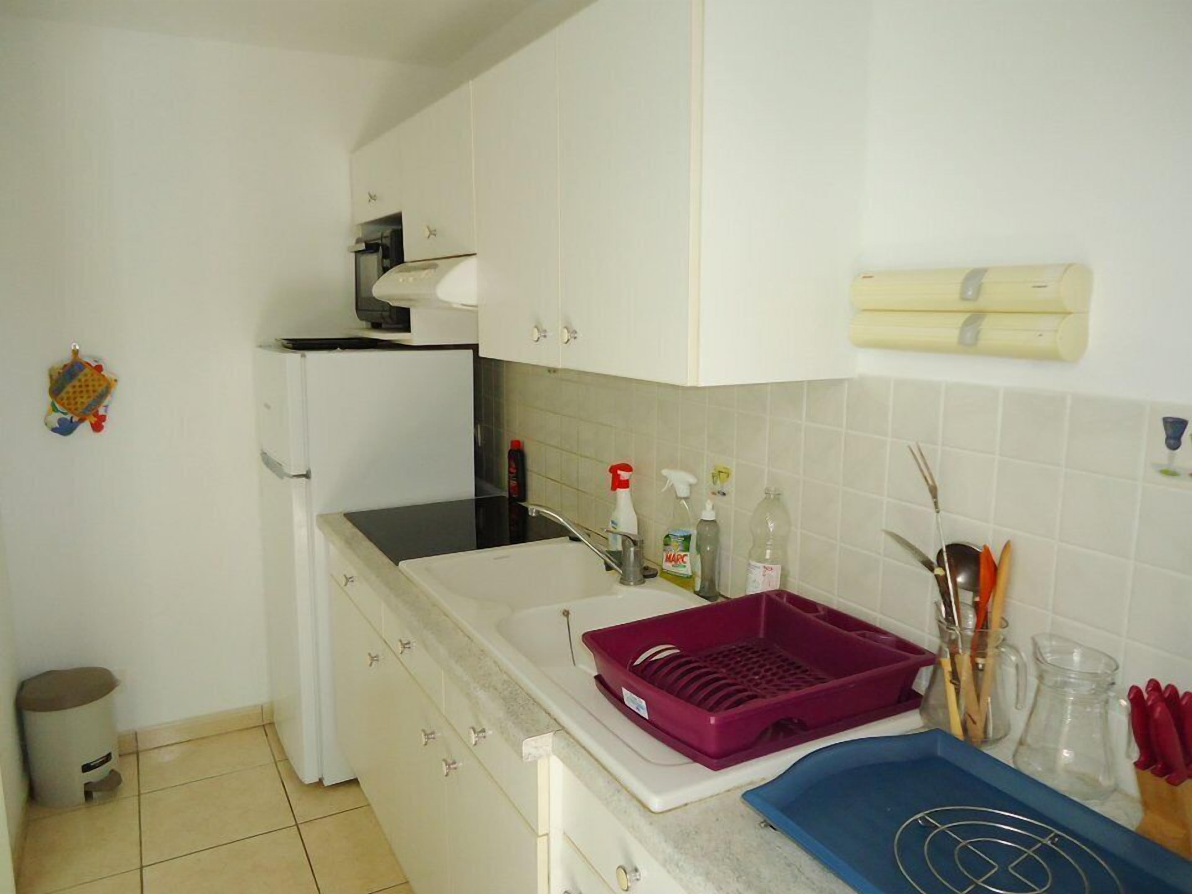 Cocina con alacenas blancas, encimera negra, pileta y diversos utensilios de cocina.