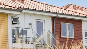 A building with a white and red exterior, numbered 24, featuring a staircase and a door with a window. - Gudhjem Søpark Lejl. 24 (Gudhjem)