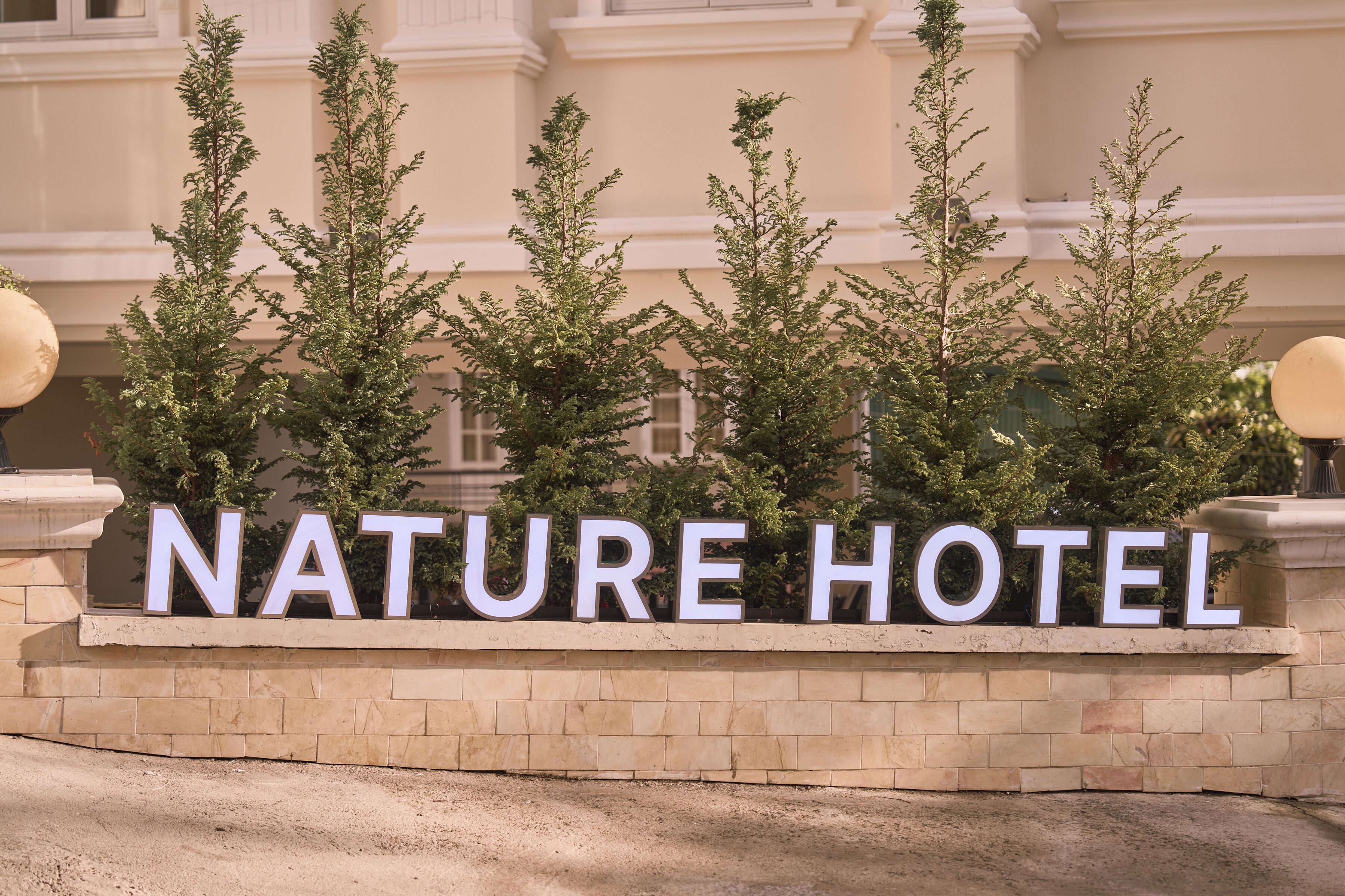 Une enseigne pour l’hôtel Nature, avec un mur de pierres et de la verdure devant.