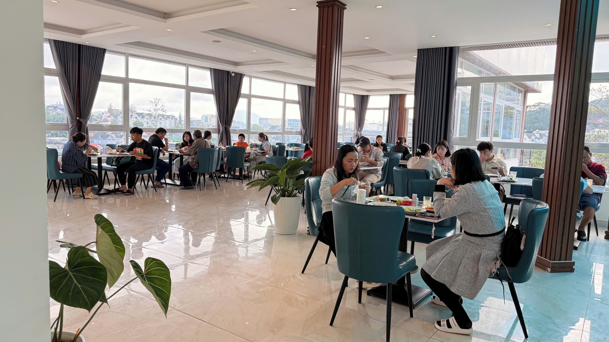 A spacious dining area with large windows, modern furniture, and potted plants.