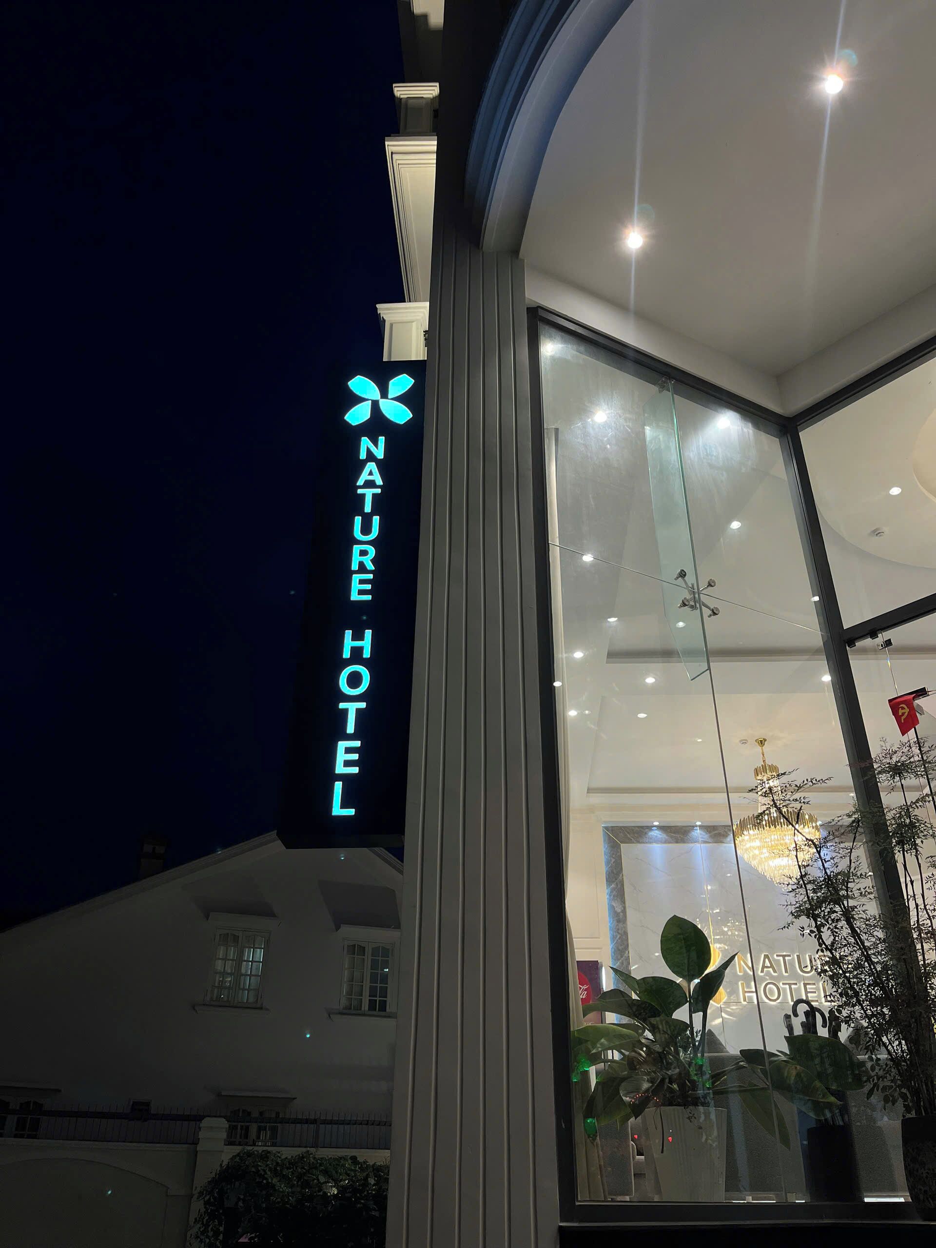 Ein Hotel mit einem auffälligen Schild 'NATURE HOTEL', großen Glasfenstern und Zimmerpflanzen.