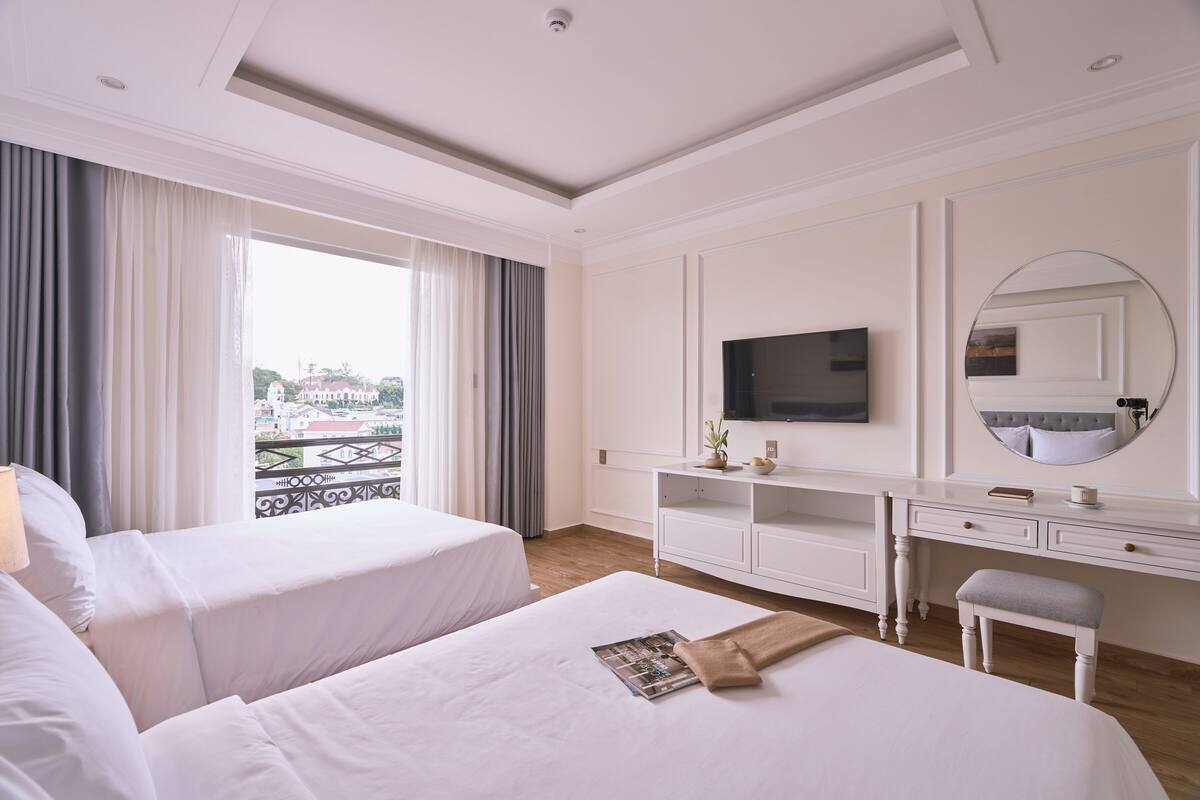 Habitación de hotel con dos camas, televisión, escritorio y vistas al balcón.