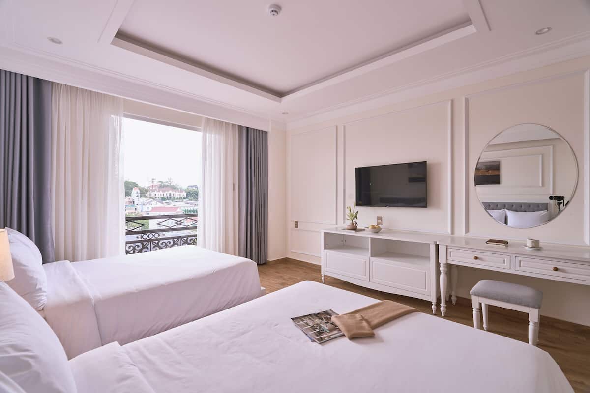A hotel room with two beds, a TV, a desk, and a balcony view.