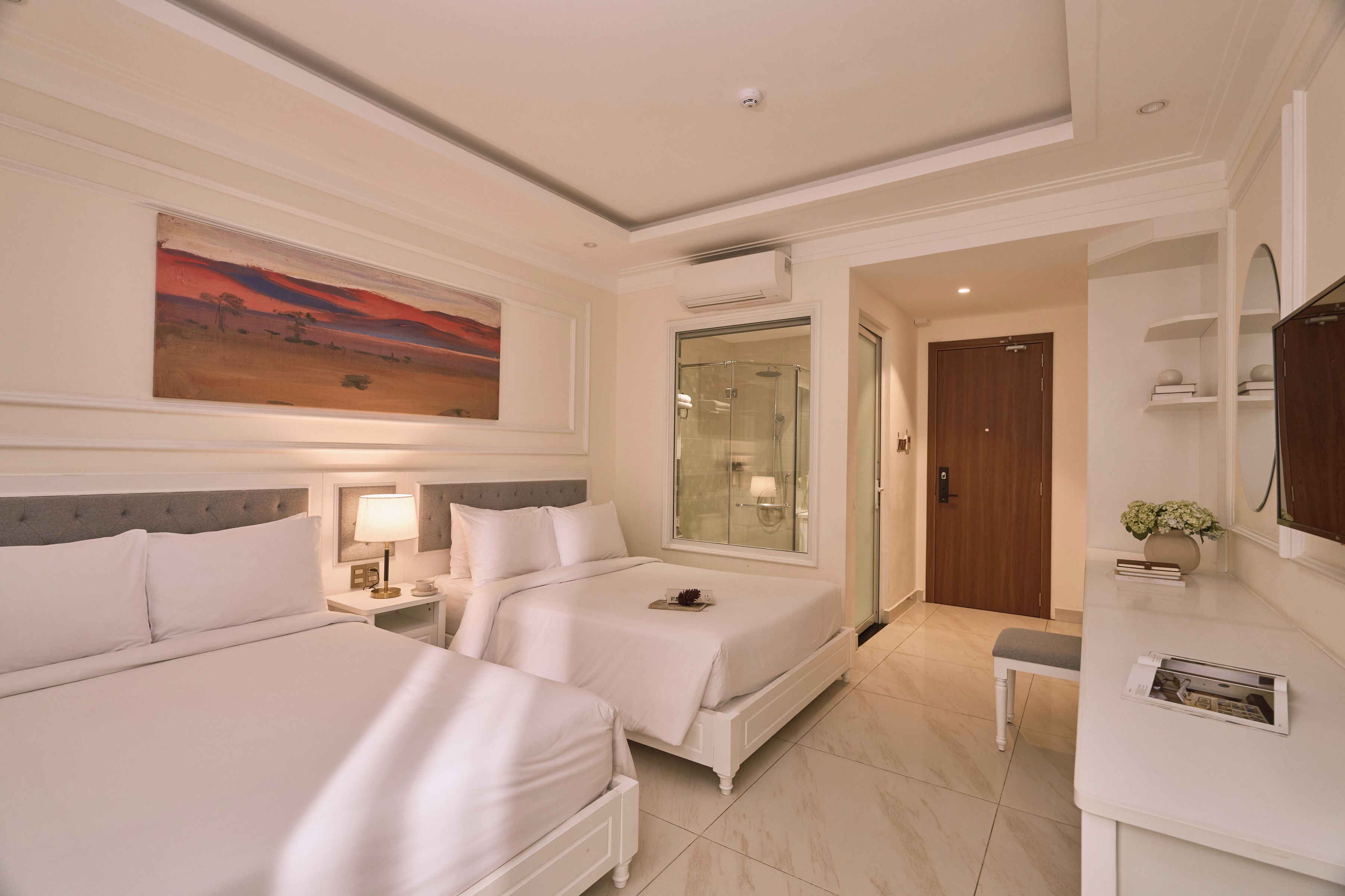 A hotel room with two beds, a large painting, a glass shower enclosure, a wooden door, and a small bench.