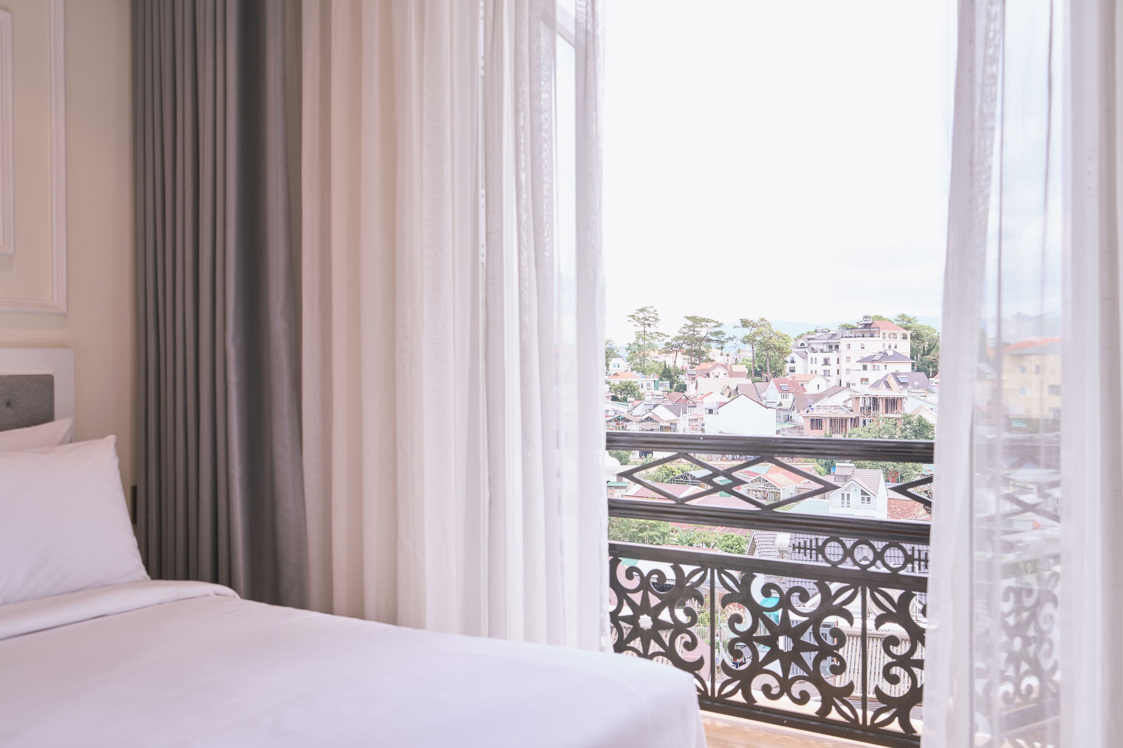 A hotel room with a bed, curtains, and a balcony with a view of buildings.