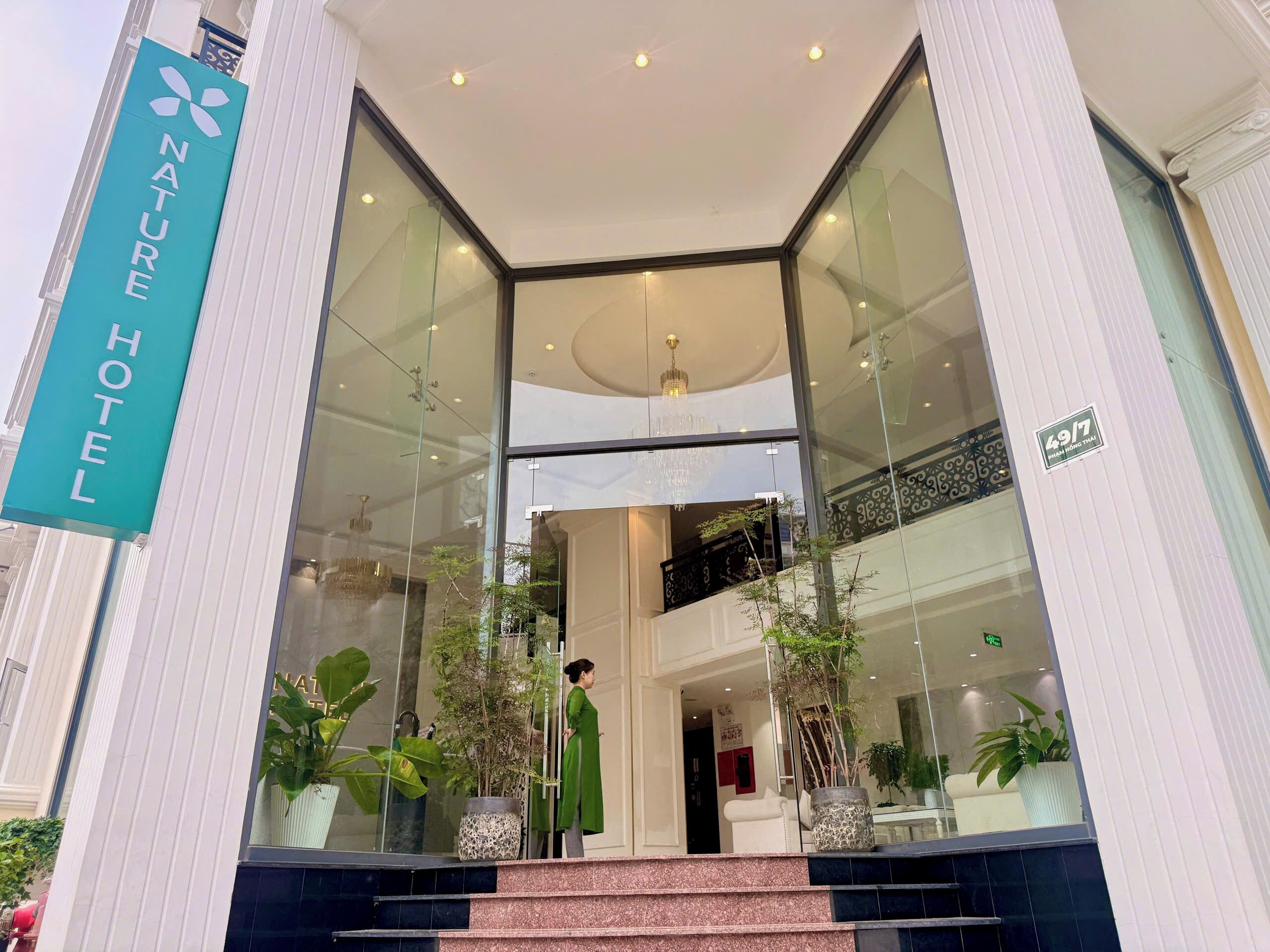 Ein Hotel Eingang mit Glasfassade, einem Schild mit der Aufschrift 'Nature Hotel' und einer Treppe, die zum Empfangsbereich führt.