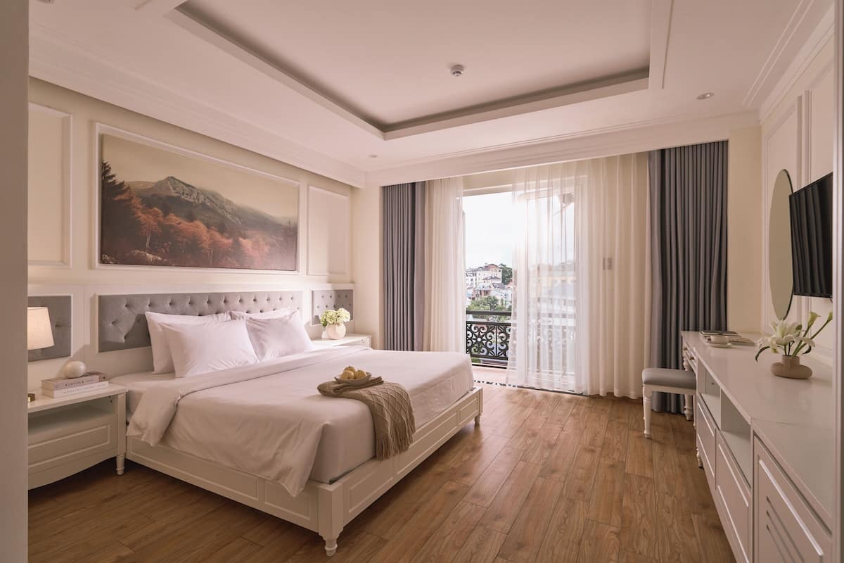 Un dormitorio con una cama grande, una mesita de noche, un aparador, un espejo y un cuadro en la pared.