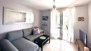 En moderne stue med en grå sofa, et lille sort sofabord, et stort spejl og et fjernsyn på et træstel.