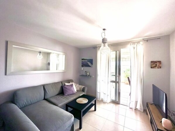A modern living room with a grey sofa, a small black coffee table, a large mirror, and a television on a wooden stand. - Apartment with large terrace in Costa Adeje. (Costa Adeje)