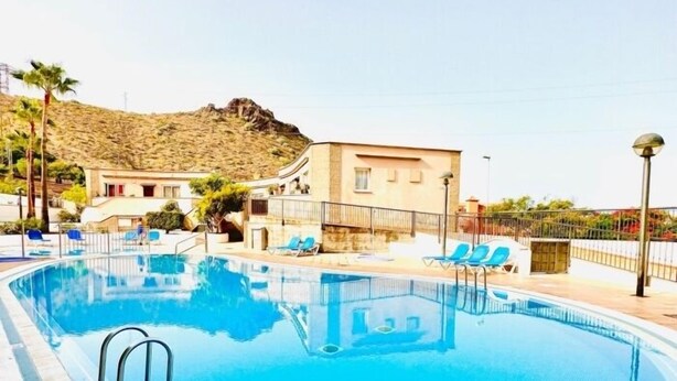 En swimmingpool med liggestole og en bygning i baggrunden.