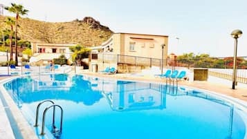 En swimmingpool med liggestole og en bygning i baggrunden.