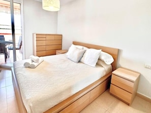 Quarto com cama, mesas de cabeceira, painel de cama em madeira e uma janela.
