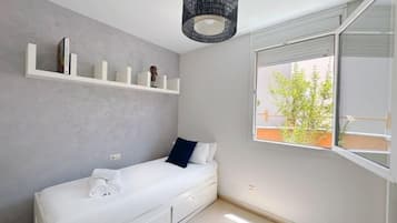 Un dormitorio minimalista con una cama individual, una ventana que da a vistas de vegetación y una estantería con libros y una pequeña figurita.
