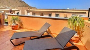 En tagterrasse med to liggestole, plantekasser og udsigt til et bjerg.